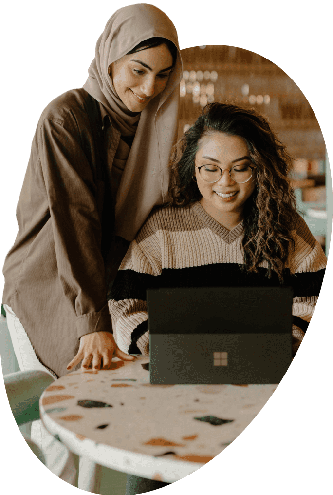 Two women smile while looking at a laptop on a table.
